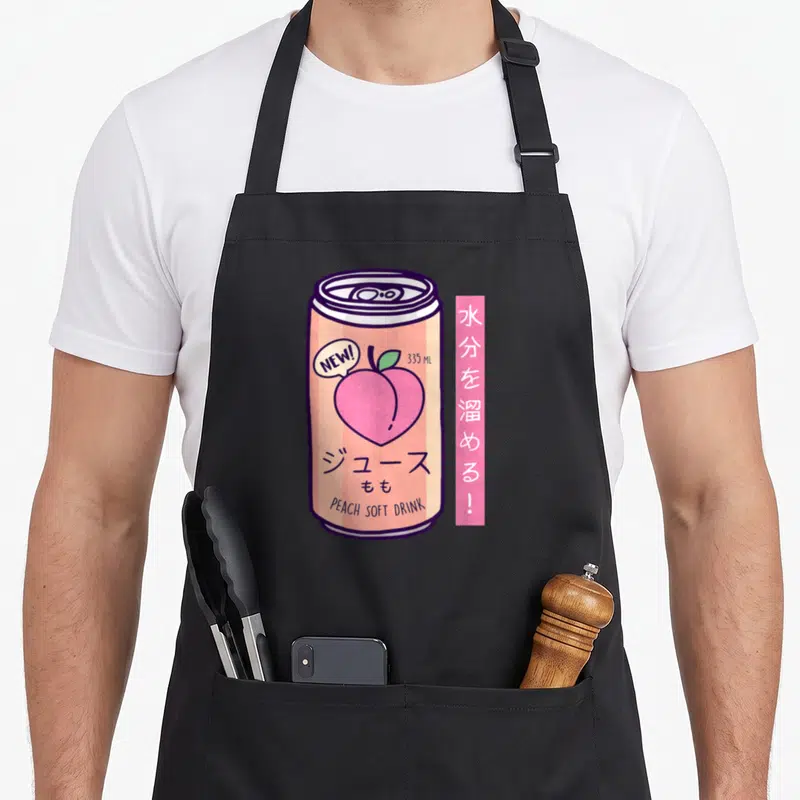 90s japan apron - Retro peach soft drink can illustration with Japanese text and pink vertical label — shown on a black cotton canvas apron against a white background