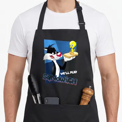 Sylvester crazy bunny man apron - Sylvester holding bread with Tweety standing on top and We'll Play Sandwich text — shown on a black cotton canvas apron against a white background