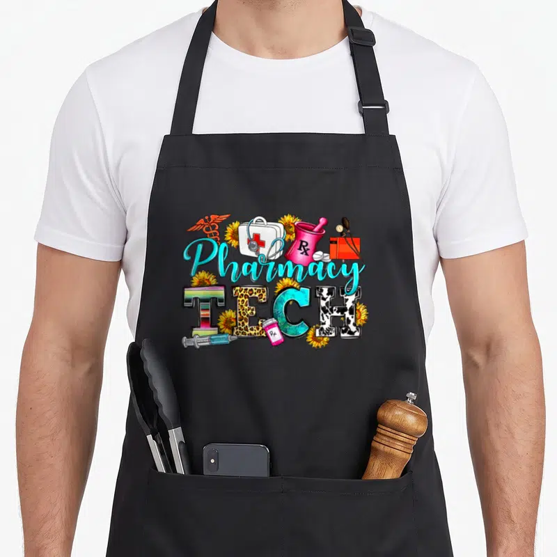Leopard pharmacist apron - Pharmacy TECH text with leopard print E, medical icons, and sunflowers in blue pink yellow — shown on a black cotton canvas apron against a white background