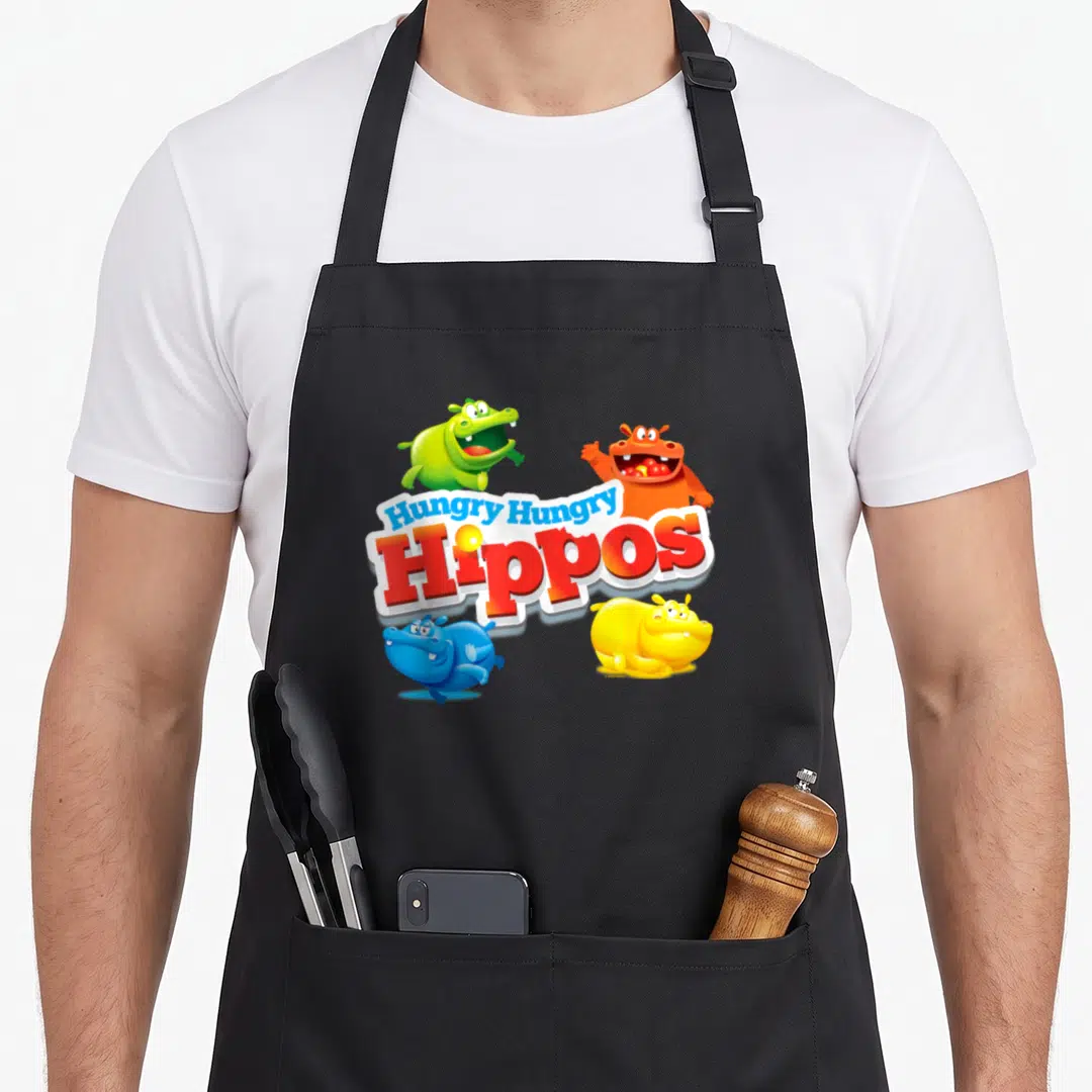 Bottomless veggie apron - Four cartoon hippos in green orange blue and yellow surrounding the Hungry Hungry Hippos logo — shown on a black cotton canvas apron against a white background