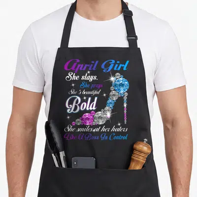 She april apron - April Girl She Slays text and diamond high heel shoe in purple blue white — shown on a black cotton canvas apron against a white background