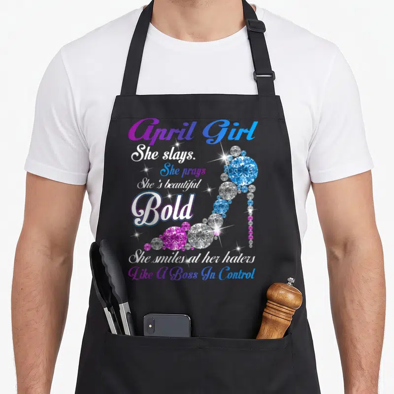 She april apron - April Girl She Slays text and diamond high heel shoe in purple blue white — shown on a black cotton canvas apron against a white background