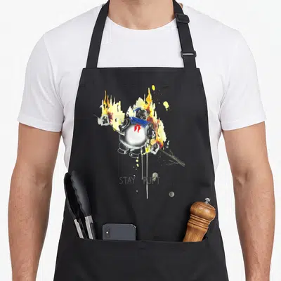 Roasted stay puft apron - Watercolor Stay Puft Marshmallow Man on fire with branch and STAY PUFT text — shown on a black cotton canvas apron against a white background