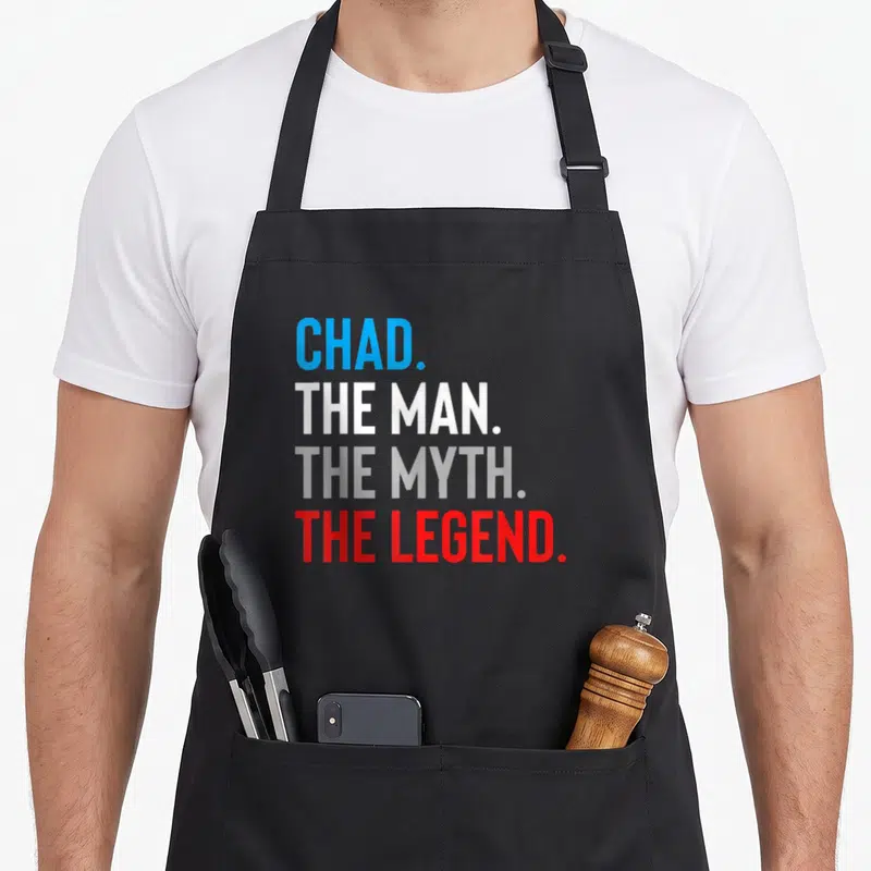 Myth chad apron - Stacked text reading CHAD THE MAN THE MYTH THE LEGEND in blue white grey and red — shown on a black cotton canvas apron against a white background