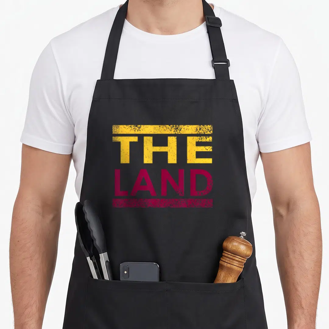 Beach modern apron - THE LAND text in yellow and maroon with distressed horizontal bars — shown on a black cotton canvas apron against a white background