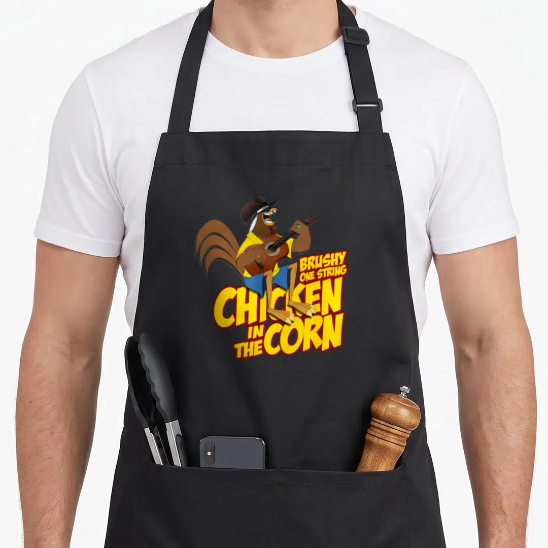 Brushy chicken apron - Cartoon rooster playing guitar above yellow text reading Brushy One String Chicken In The Corn — shown on a black cotton canvas apron against a white background