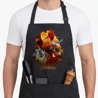 Main lion apron - Circular cartoon collage of lions, Zazu, Pumbaa, Timon, and hyenas with THE LION KING text at bottom — shown on a black cotton canvas apron against a white background