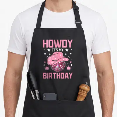 Howdy cowgirl aprons - Pink cowboy hat on disco ball with stars and birthday text — shown on a black cotton canvas apron against a white background