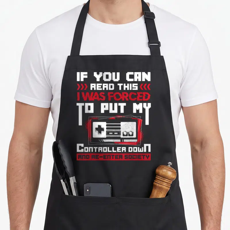 Controller gaming apron - Pixelated white and red text with retro game controller illustration and sarcasm quote — shown on a black cotton canvas apron against a white background