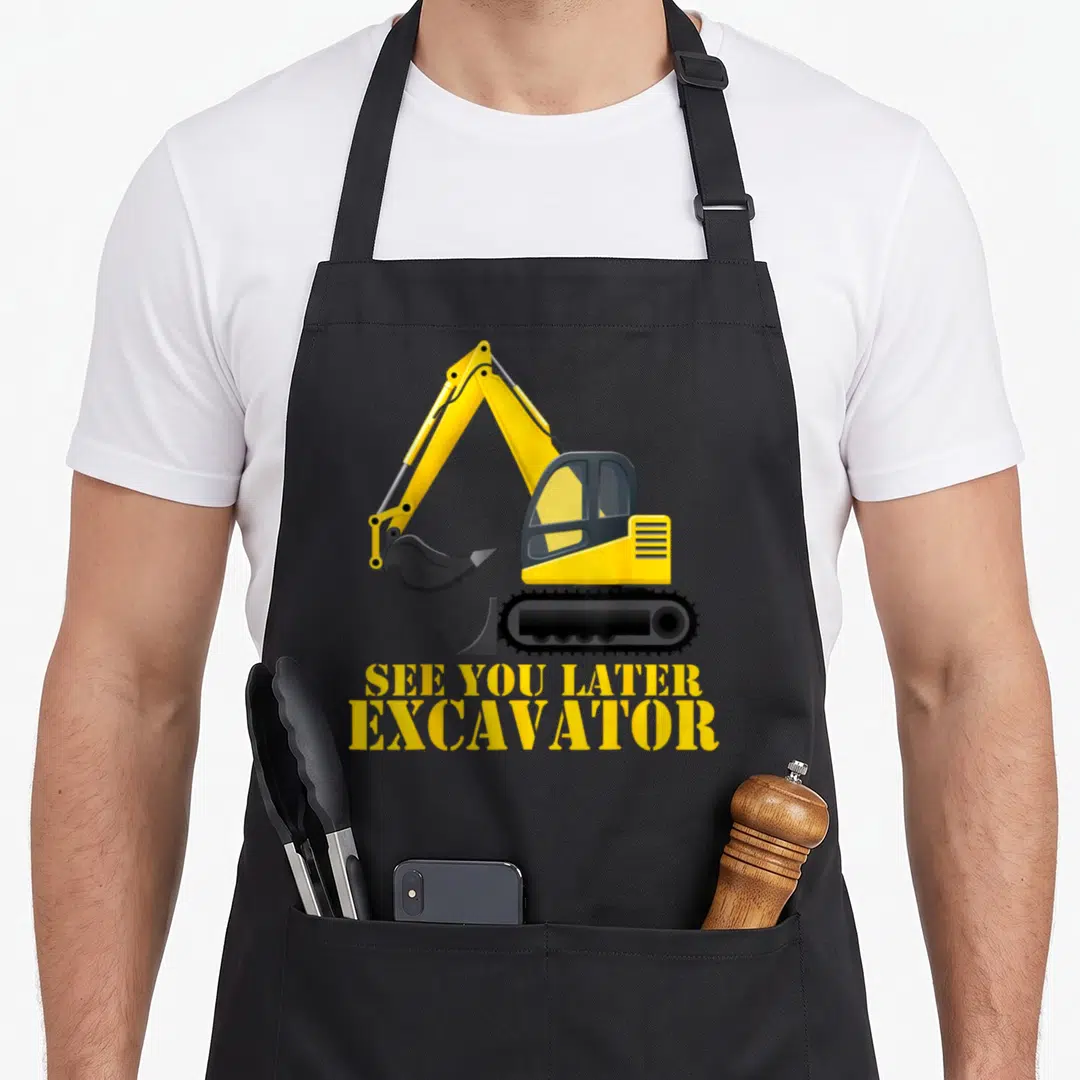 See excavator girl apron - Yellow cartoon excavator above SEE YOU LATER EXCAVATOR text in stencil font — shown on a black cotton canvas apron against a white background