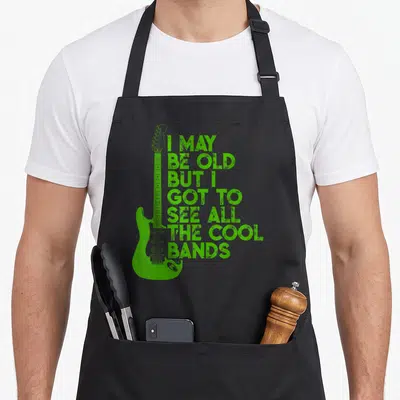 But vintage may apron - Green electric guitar with stacked distressed text reading I may be old but I got to see all — shown on a black cotton canvas apron against a white background