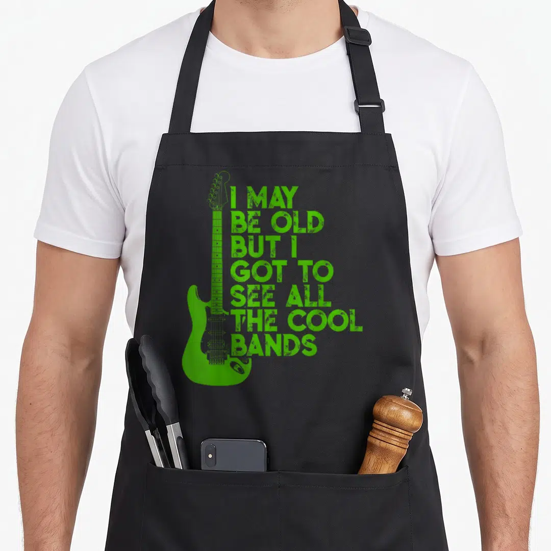 But vintage may apron - Green electric guitar with stacked distressed text reading I may be old but I got to see all — shown on a black cotton canvas apron against a white background