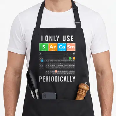 Use table apron - I Only Use S Ar Ca Sm Periodically text with green orange blue red tiles over grey periodic table — shown on a black cotton canvas apron against a white background