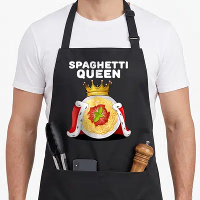 Queen pasta apron - Cartoon plate of spaghetti topped with gold crown and red royal cape with white text — shown on a black cotton canvas apron against a white background