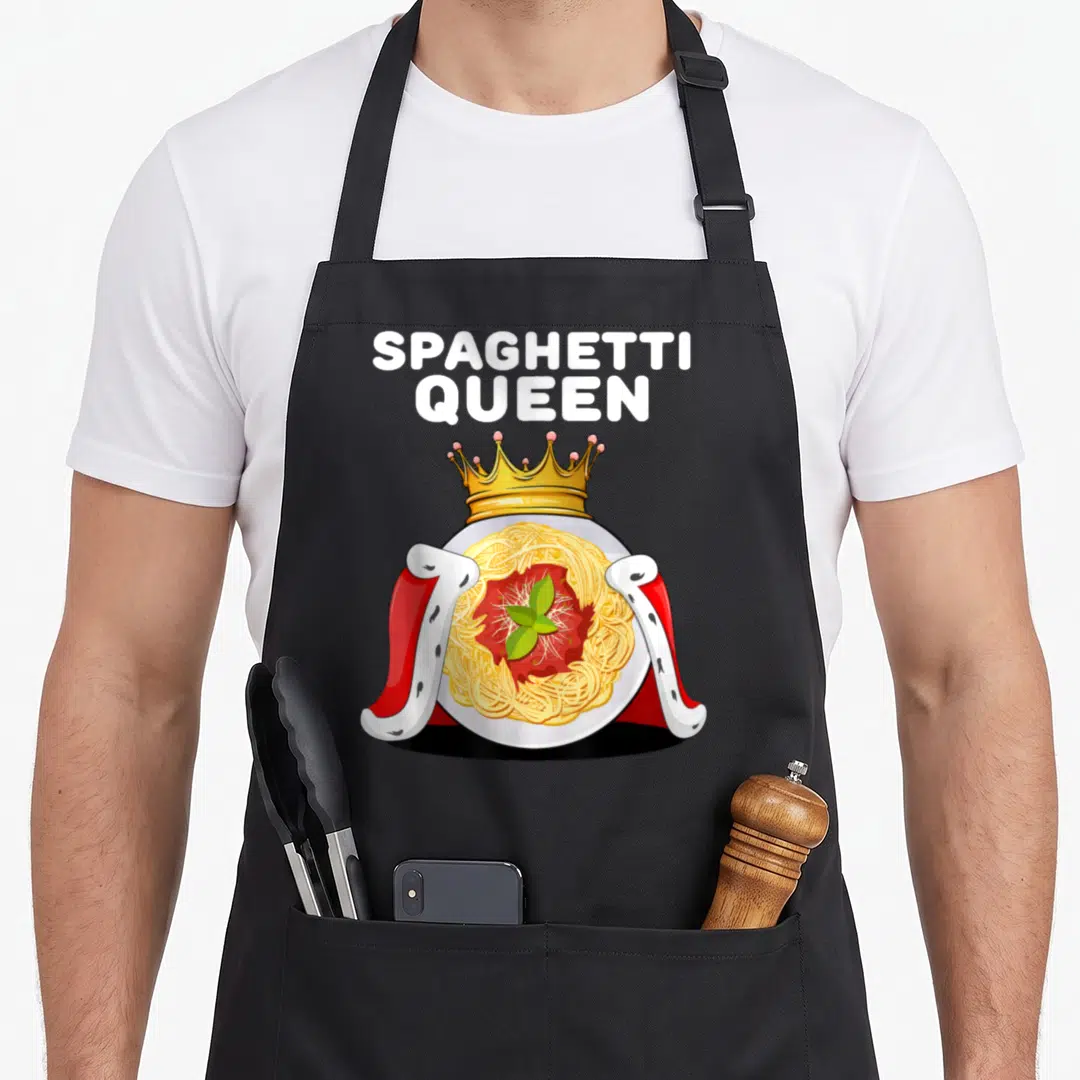 Queen pasta apron - Cartoon plate of spaghetti topped with gold crown and red royal cape with white text — shown on a black cotton canvas apron against a white background