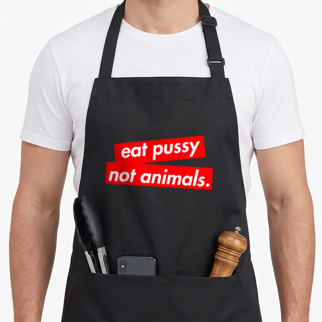 Animal vegan apron - White text eat pussy not animals on stacked red rectangular bars — shown on a black cotton canvas apron against a white background