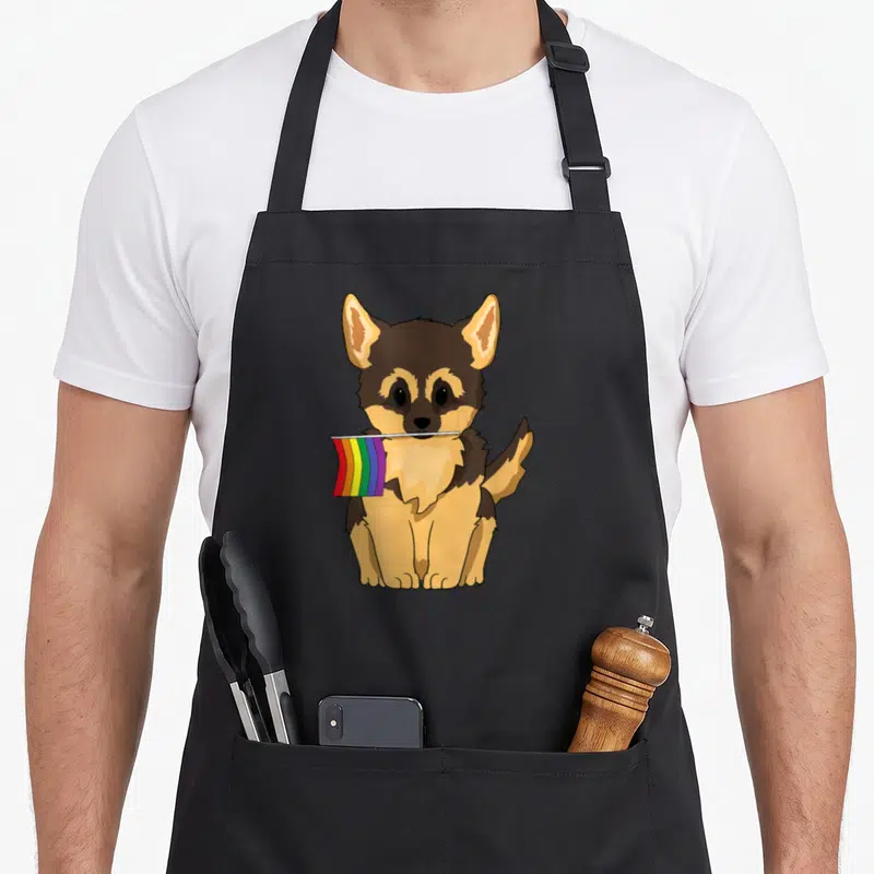 German gay pride apron - Cartoon German Shepherd puppy sitting holding a red orange yellow green blue purple rainbow — shown on a black cotton canvas apron against a white background