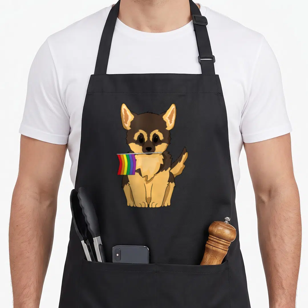 German gay pride apron - Cartoon German Shepherd puppy sitting holding a red orange yellow green blue purple rainbow — shown on a black cotton canvas apron against a white background