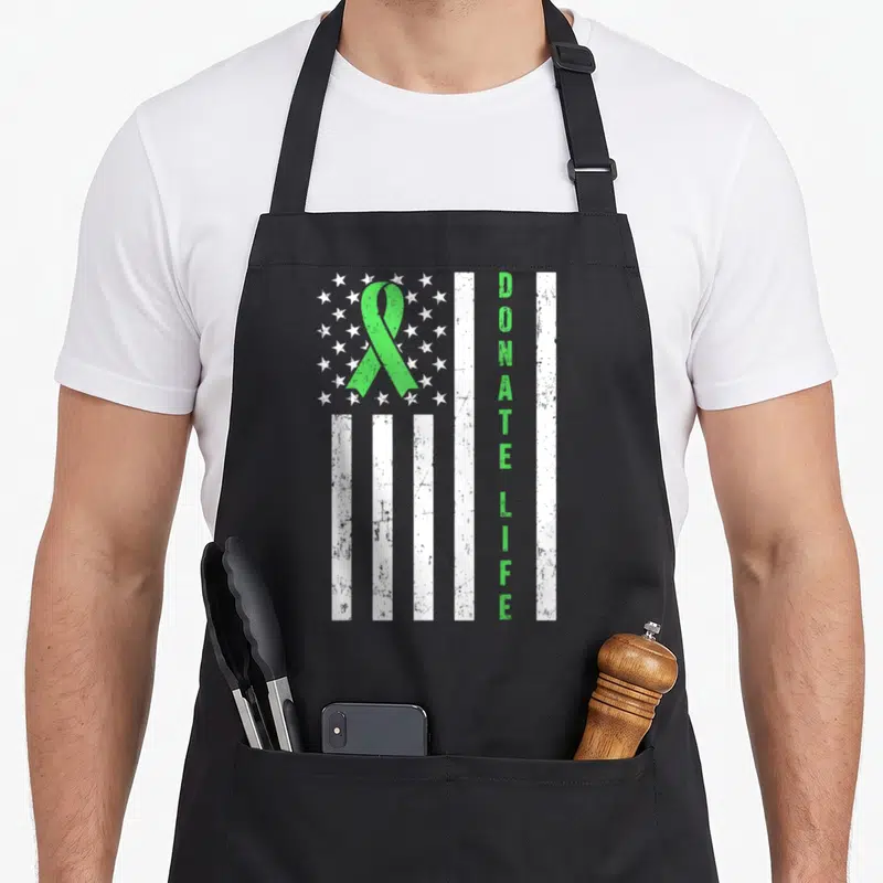Donor awareness organ apron - Green ribbon over white stars and stripes with vertical DONATE LIFE text in distressed — shown on a black cotton canvas apron against a white background