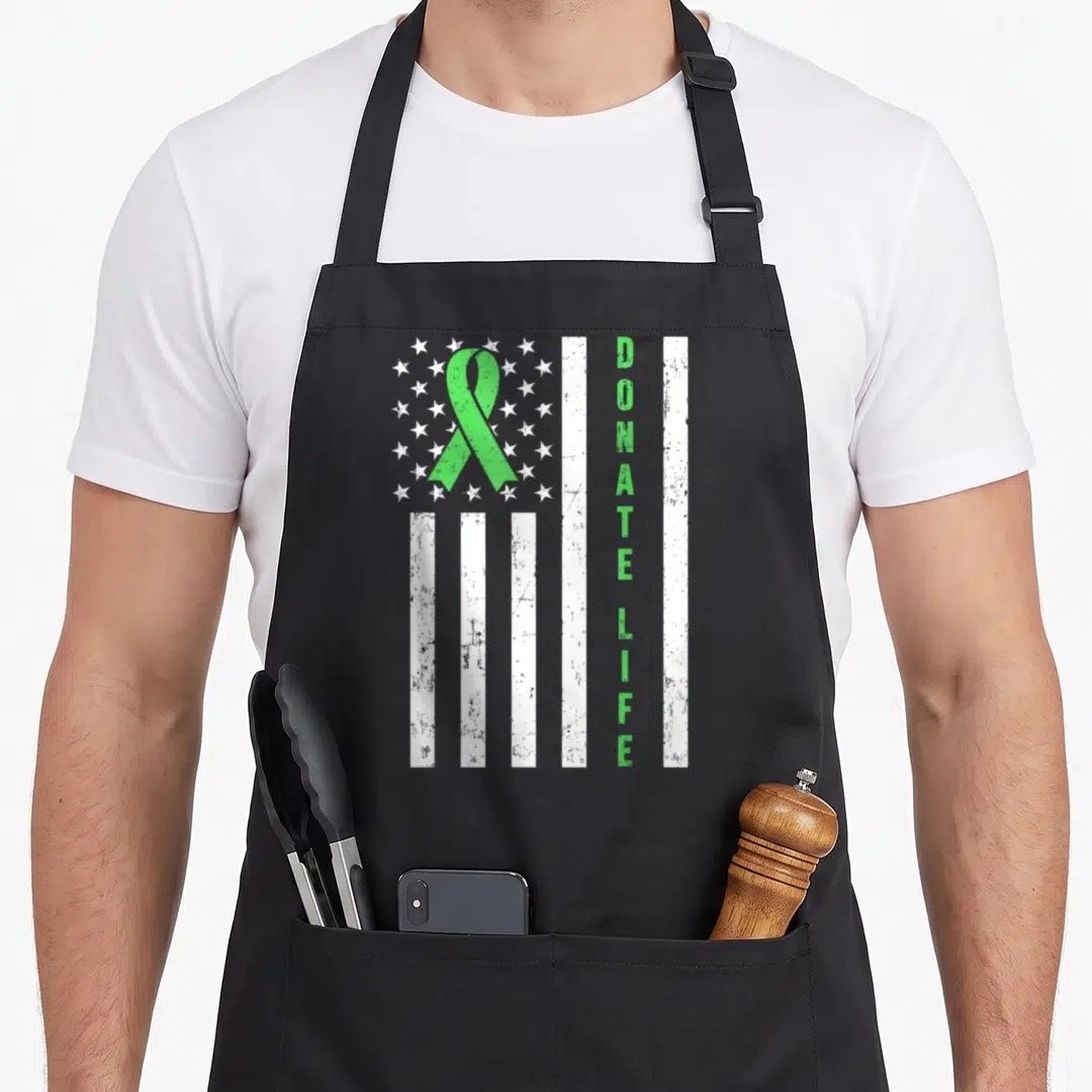Donor awareness organ apron - Green ribbon over white stars and stripes with vertical DONATE LIFE text in distressed — shown on a black cotton canvas apron against a white background