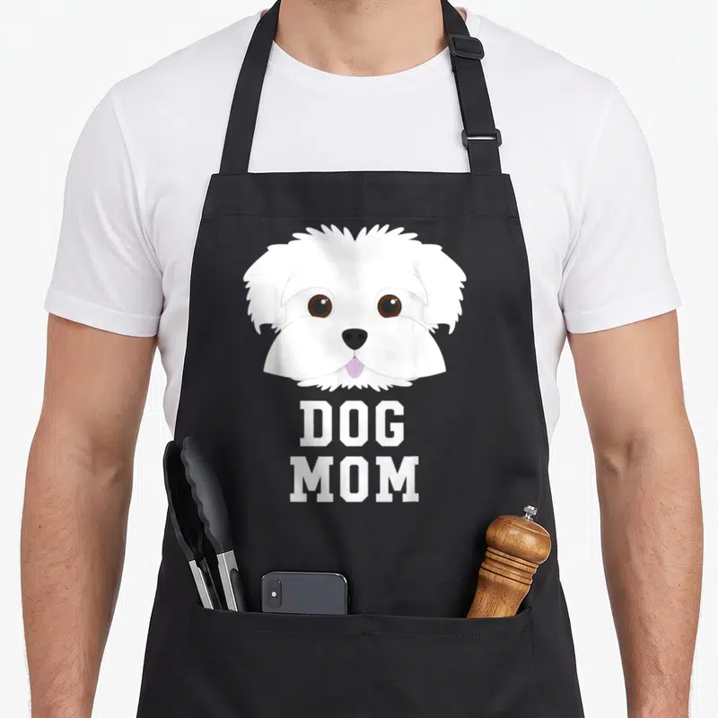 Dog maltese mother's day aprons - Cartoon white dog head above DOG MOM text in block letters — shown on a black cotton canvas apron against a white background