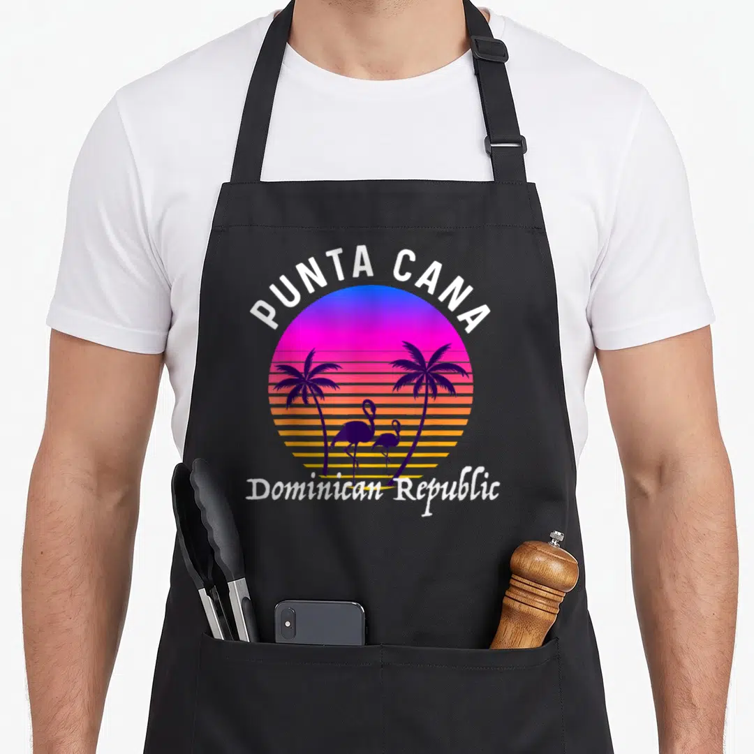 Souvenir family aprons - Retro sunset circle with PUNTA CANA text, two palm trees, two flamingos, and horizontal — shown on a black cotton canvas apron against a white background