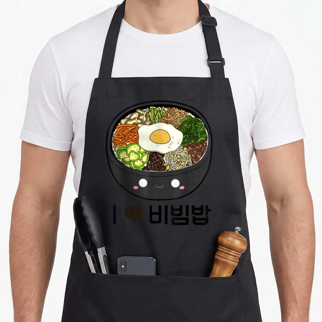 Bibimbap korean apron - Cartoon bibimbap bowl with face and I love bibimbap text — shown on a black cotton canvas apron against a white background