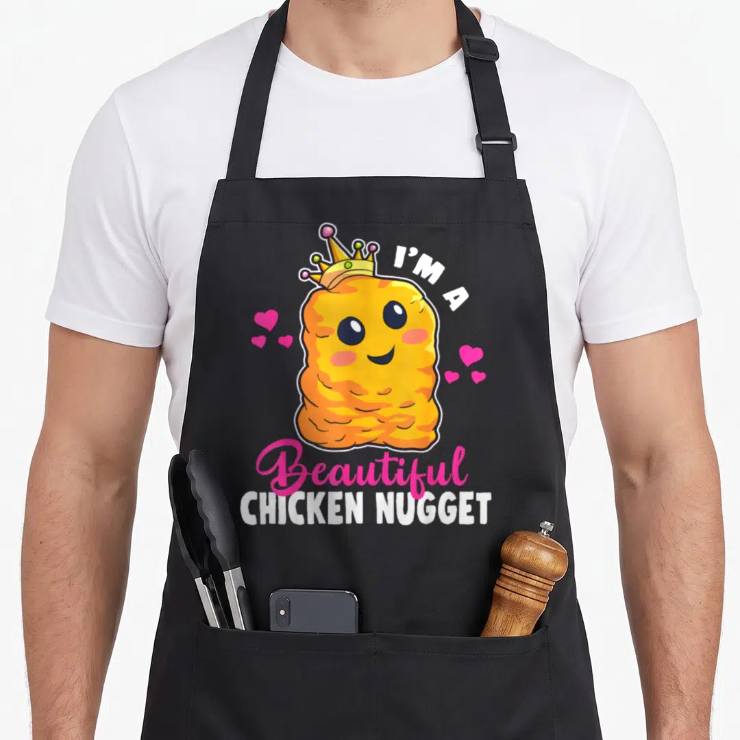 Kawaii chicken print apron - Cartoon orange nugget wearing a gold crown surrounded by pink hearts with white and pink — shown on a black cotton canvas apron against a white background