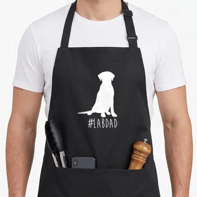 Hashtag labrador apron - White sitting dog silhouette above #LABDAD text — shown on a black cotton canvas apron against a white background