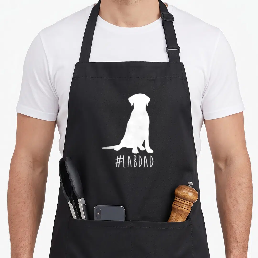 Hashtag labrador apron - White sitting dog silhouette above #LABDAD text — shown on a black cotton canvas apron against a white background