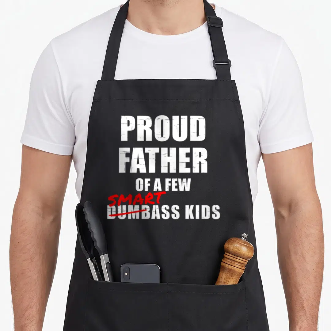 Father proud dad apron - Stacked white text reading Proud Father Of A Few Smart Dumbass Kids with red cross-out — shown on a black cotton canvas apron against a white background