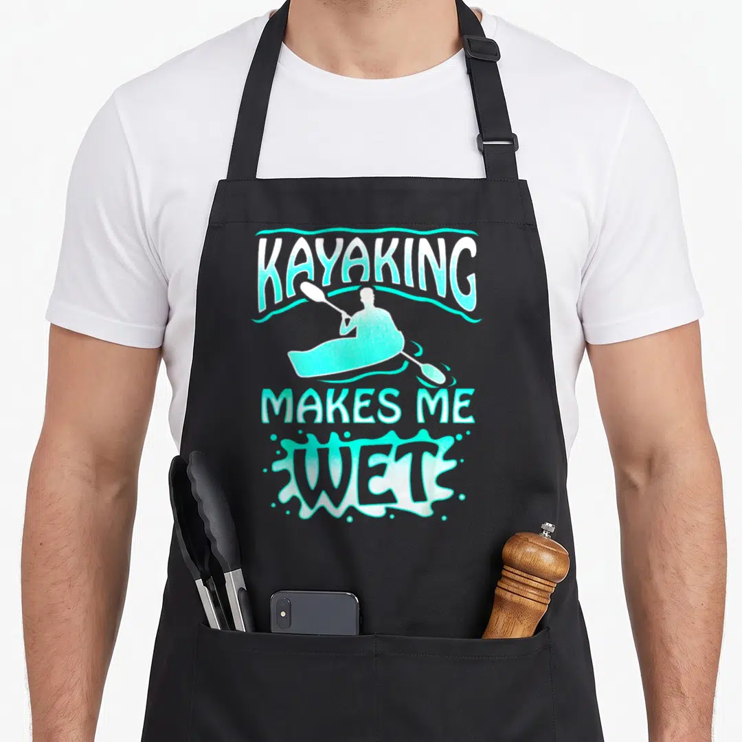 Watersport wet aprons - Cartoon kayaker silhouette with KAYAKING MAKES ME WET text in turquoise and white splash shape — shown on a black cotton canvas apron against a white background