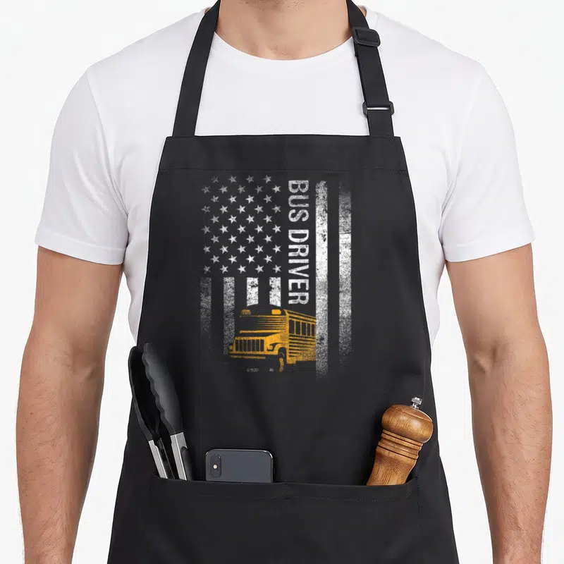 School american flag apron - Yellow school bus under vertical BUS DRIVER text over white distressed stars and stripes — shown on a black cotton canvas apron against a white background
