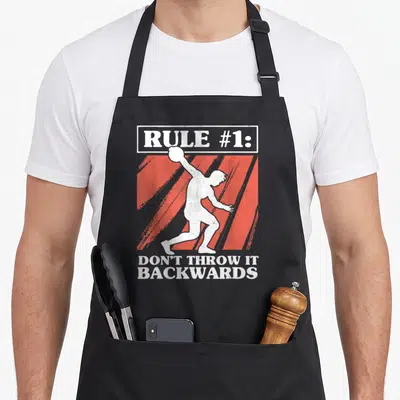 Rule discus apron - Rugby player silhouette over red stripes with text don't throw it backwards — shown on a black cotton canvas apron against a white background