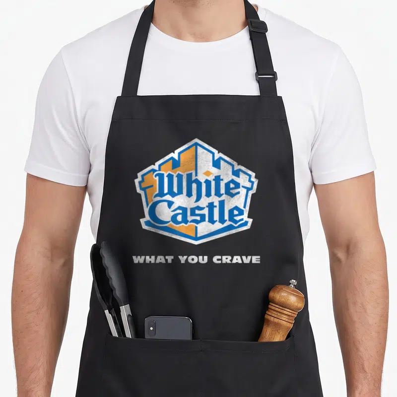 Distressed white castle apron - Blue and orange castle emblem with white 'WHAT YOU CRAVE' text in distressed style — shown on a black cotton canvas apron against a white background