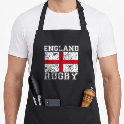 Flag england rugby apron - Distressed red and white flag with ENGLAND above and RUGBY below — shown on a black cotton canvas apron against a white background