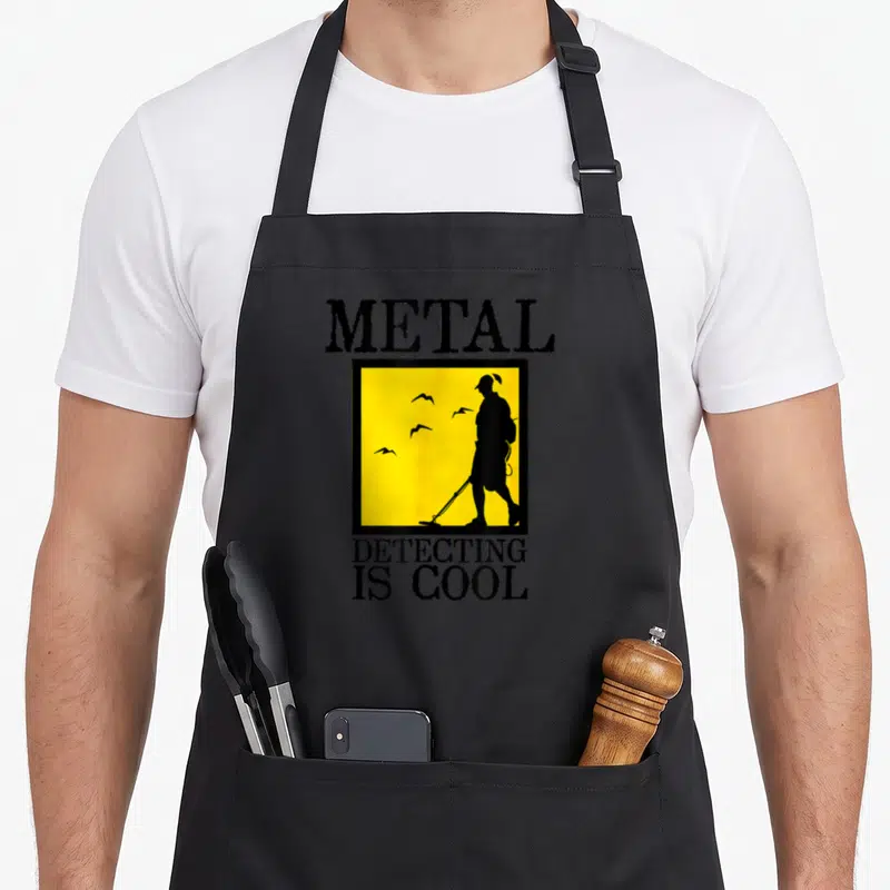 Funny detector metal detecting apron - Black text metal detecting is cool above a yellow square containing — shown on a black cotton canvas apron against a white background