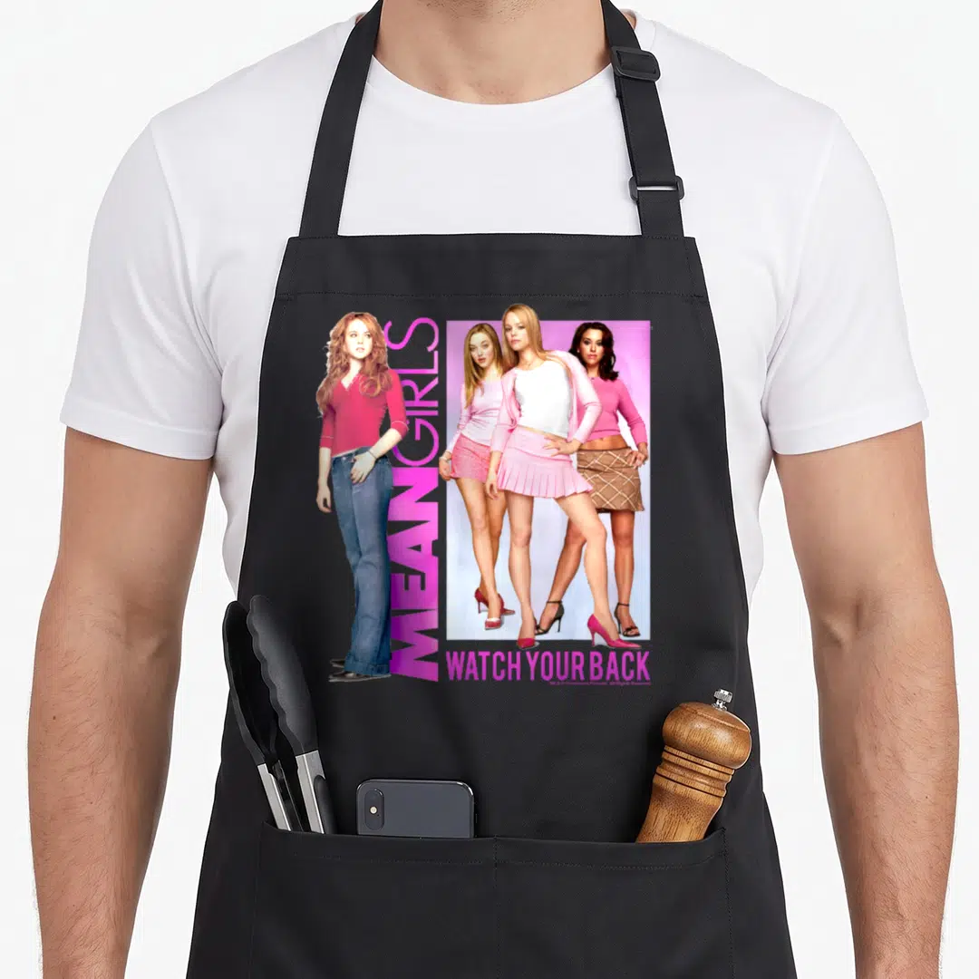 Watch mean girls apron - Four women posed near pink rectangle with vertical MEAN GIRLS and horizontal WATCH YOUR BACK — shown on a black cotton canvas apron against a white background