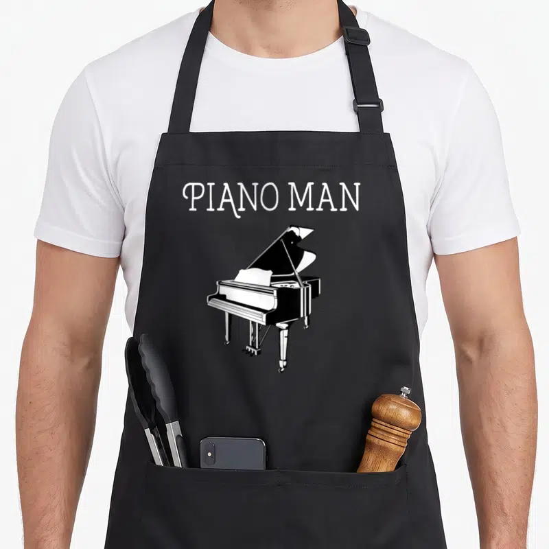 Player pianist piano apron - PIANO MAN text above white grand piano line art on black — shown on a black cotton canvas apron against a white background