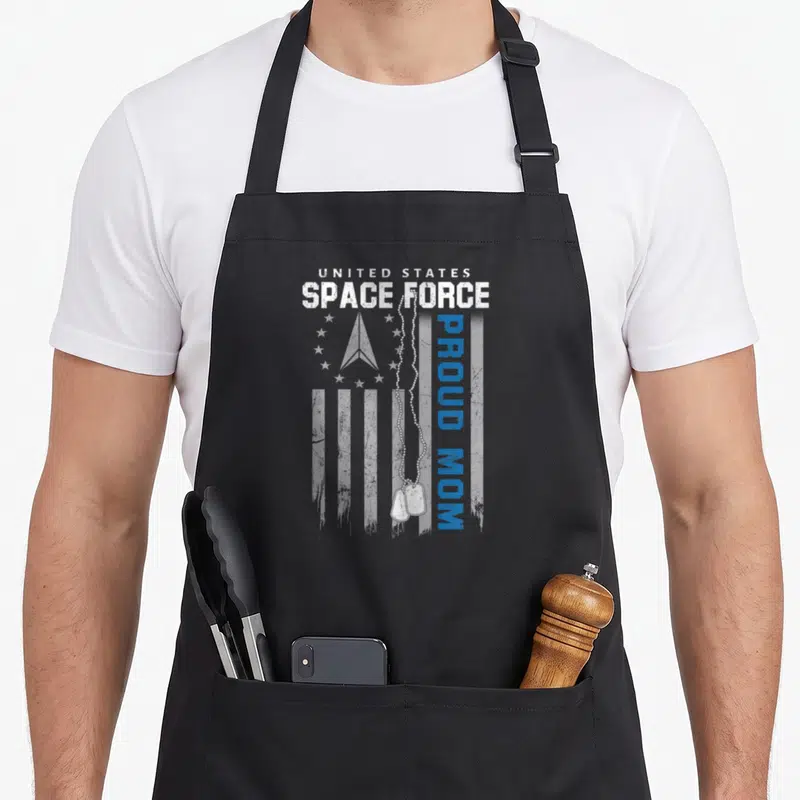 Proud space family aprons - US Space Force emblem, white flag stripes, blue Proud Mom text, and hanging dog tags — shown on a black cotton canvas apron against a white background