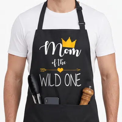 Wild baby birthday apron - White Mom of the Wild One text with yellow crown and heart arrow — shown on a black cotton canvas apron against a white background