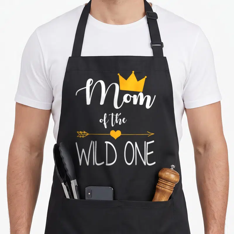 Wild baby birthday apron - White Mom of the Wild One text with yellow crown and heart arrow — shown on a black cotton canvas apron against a white background