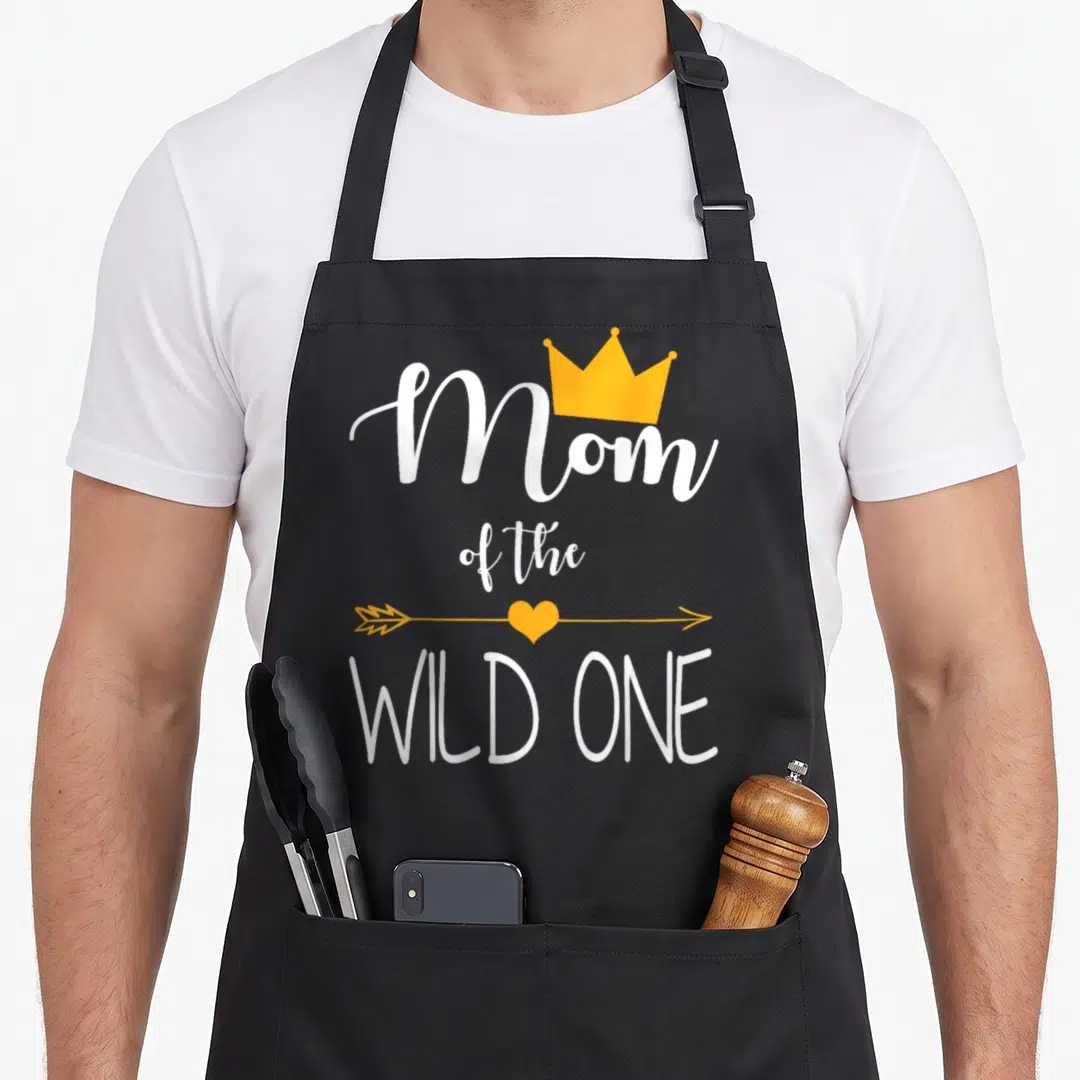 Wild baby birthday apron - White Mom of the Wild One text with yellow crown and heart arrow — shown on a black cotton canvas apron against a white background