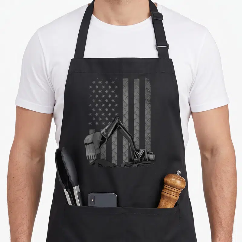Patriotic construction worker apron - Distressed grey and black excavator on a diamond plate flag background — shown on a black cotton canvas apron against a white background