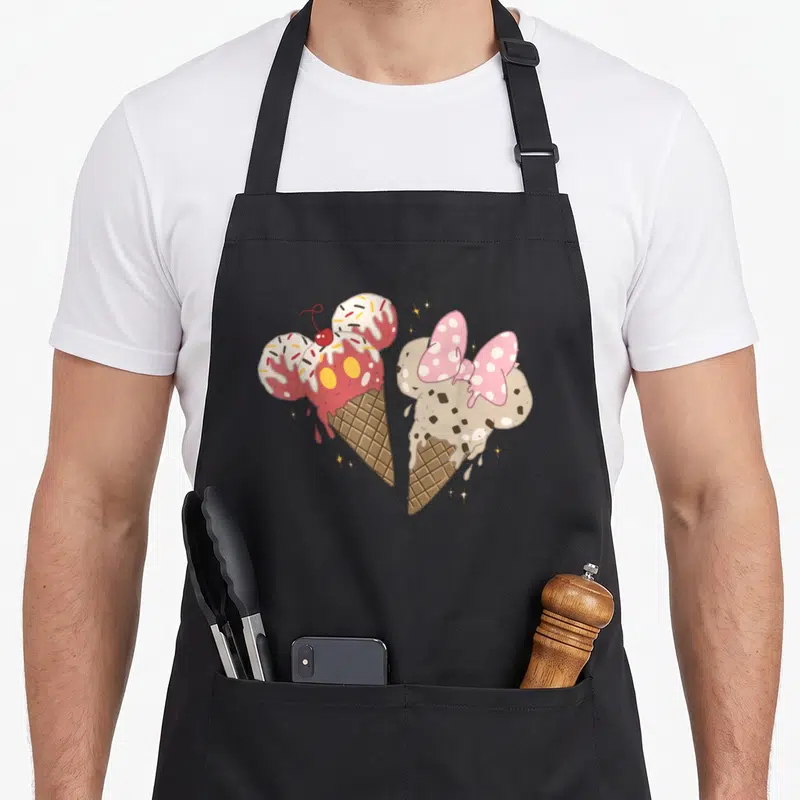 Friend ice cream apron - Two cartoon mouse-shaped ice cream cones with gold stars in pink beige and brown — shown on a black cotton canvas apron against a white background
