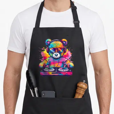 Teddy cartoon apron - Multicolored bear wearing headphones and sunglasses behind a DJ controller with paint splashes — shown on a black cotton canvas apron against a white background