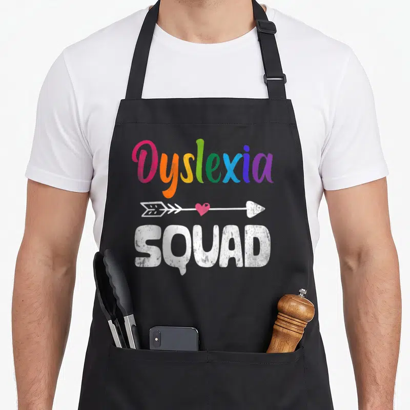 Awareness teacher apron - Rainbow Dyslexia text above white arrow with pink heart and SQUAD below — shown on a black cotton canvas apron against a white background
