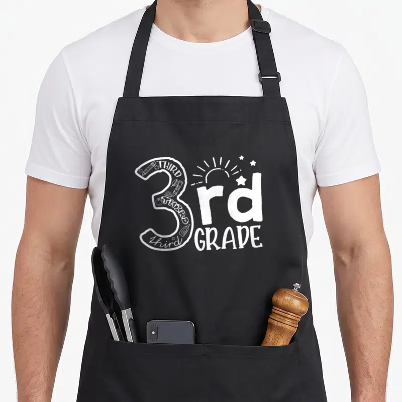 Squad third teacher apron - Large number 3 filled with pencils crayons and stars next to rd GRADE text — shown on a black cotton canvas apron against a white background