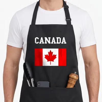 Flag canadian aprons - White CANADA text above a distressed red and white rectangular Canadian flag with maple leaf — shown on a black cotton canvas apron against a white background