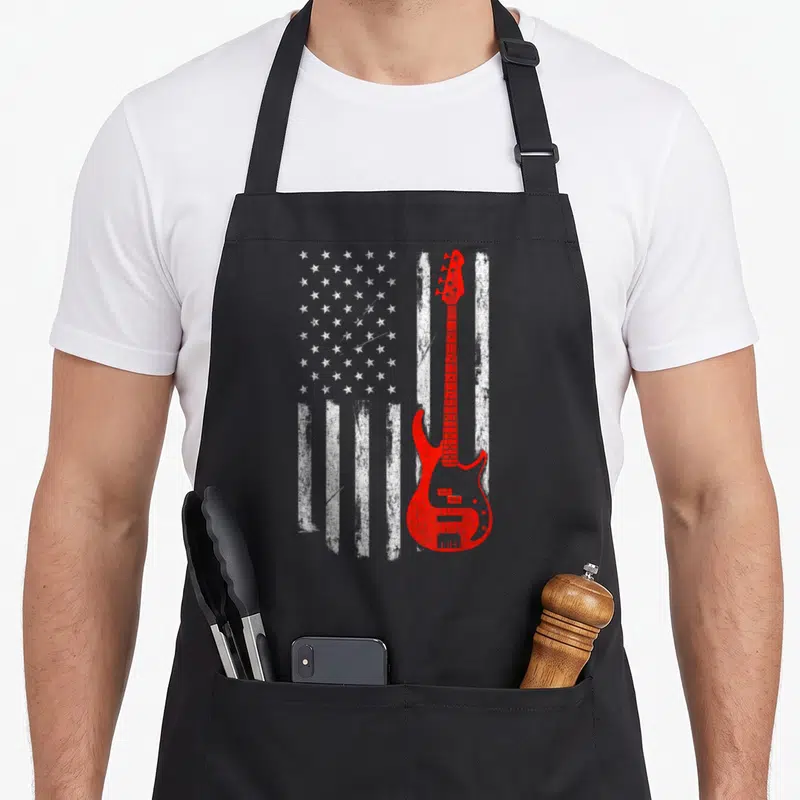 Bassist american flag apron - Red bass guitar silhouette over distressed white stars and stripes pattern — shown on a black cotton canvas apron against a white background